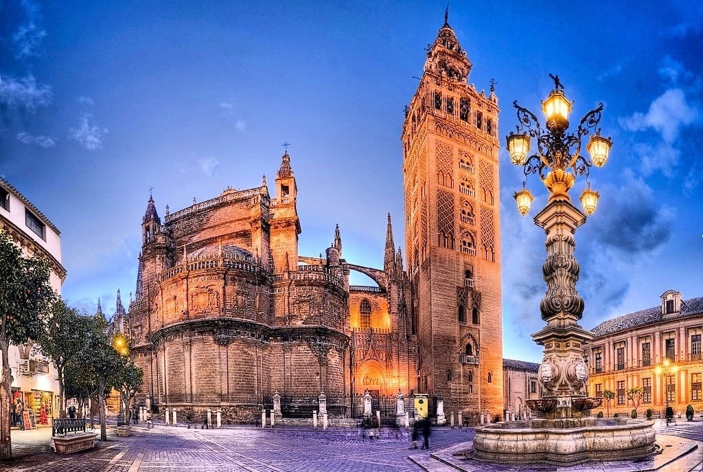 Vista da Catedral de Sevilha e da Torre da Giralda iluminadas ao entardecer na Espanha.