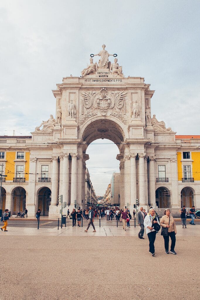 Arco da Rua Augusta em Lisboa com pessoas caminhando na Praça do Comércio ao entardecer.