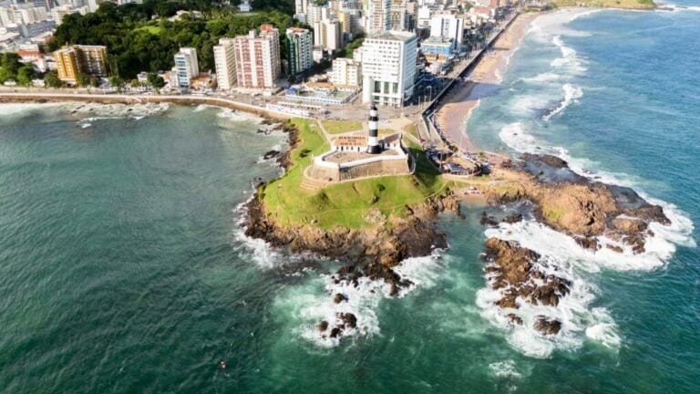 Imagem aérea do Farol da Barra em Salvador, com mar agitado ao redor e prédios ao fundo. Roteiro de 5 dias em Salvador.