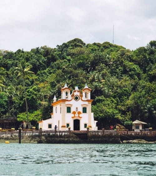 Igreja de Nossa Senhora de Guadalupe rodeada por mata atlântica na Ilha dos Frades, em Salvador, vista do mar. Roteiro de 5 dias em Salvador.