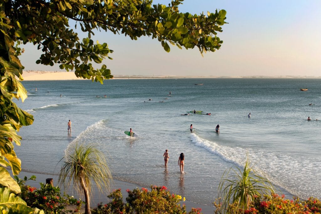 Praia de Jericoacoara com banhistas na areia e surfistas aproveitando as ondas no mar. Um dos destinos tendência mais bonitos do Brasil!