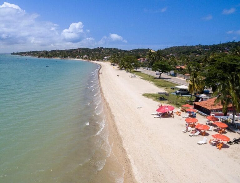 Vista aérea da Praia Ponta de Areia, em Itaparica, com mar calmo, areia clara e barracas coloridas à beira-mar. Roteiro de 5 dias em Salvador.