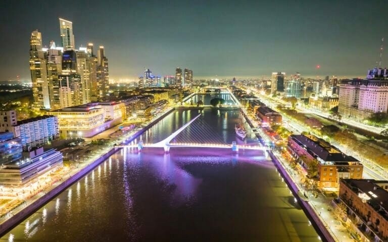 Vista noturna de Puerto Madero em Buenos Aires com a Puente de la Mujer iluminada.
