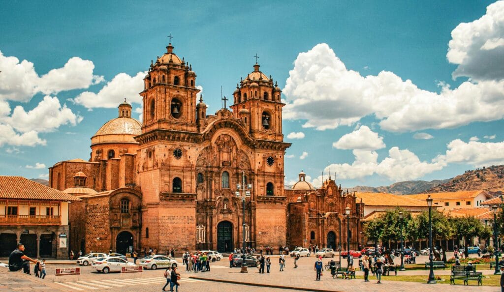 Fachada da Catedral de Cusco com turistas na Plaza de Armas e céu azul com nuvens