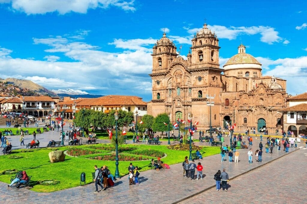 Plaza de Armas de Cusco com a Catedral e turistas caminhando em um dia ensolarado.