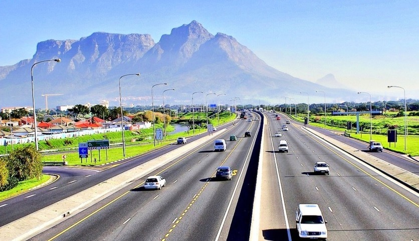 Rodovia N2 em direção ao interior da África do Sul, com diversos carros em movimento e a Table Mountain ao fundo em um dia claro.