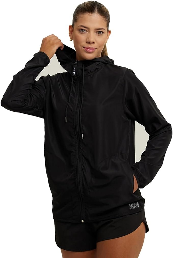 Mulher vestindo jaqueta corta-vento preta com capuz, ideal para proteção contra vento e chuva durante viagens