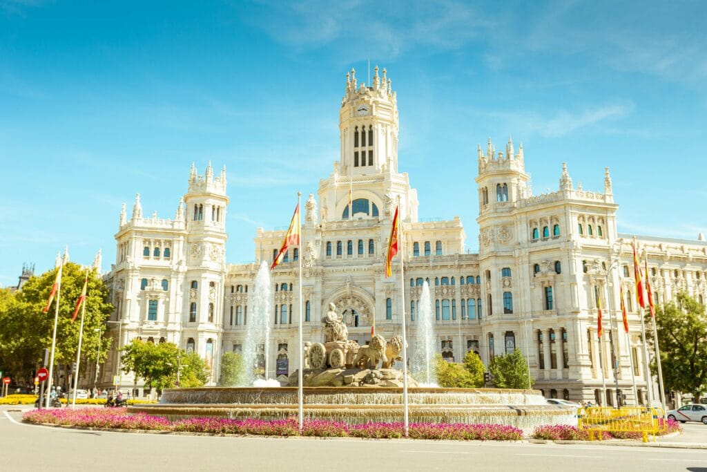Fonte de Cibeles e o Palácio de Cibeles iluminados sob o céu azul de Madri.
