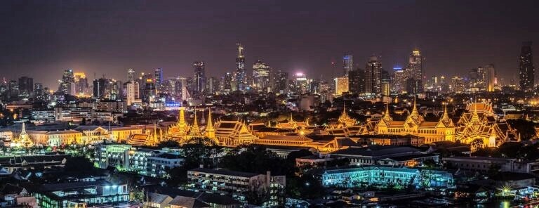 Vista noturna dos templos dourados e do Palácio Real de Bangkok com a cidade ao fundo.