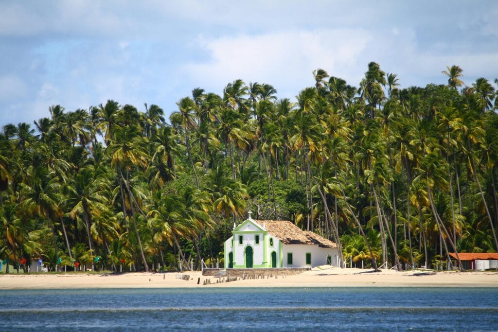 Vista do mar da Praia dos Carneiros, em Pernambuco, com destaque para a Capela de São Benedito e o coqueiral ao fundo. Um dos destinos tendência mais bonitos do Brasil!