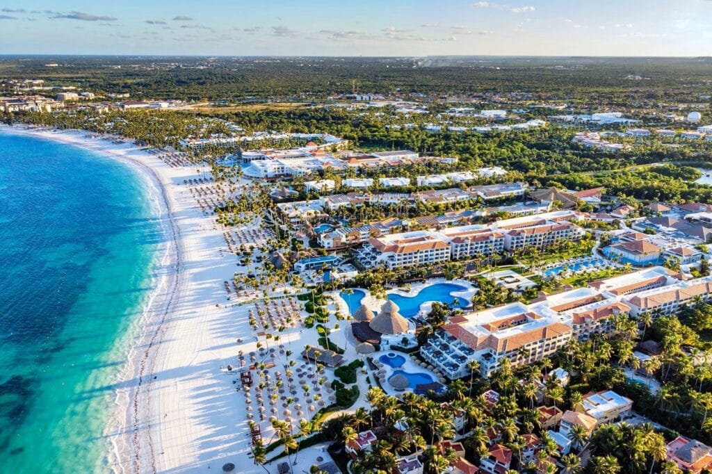 Vista aérea de praia paradisíaca em Punta Cana com águas azul-turquesa, coqueiros e barcos.