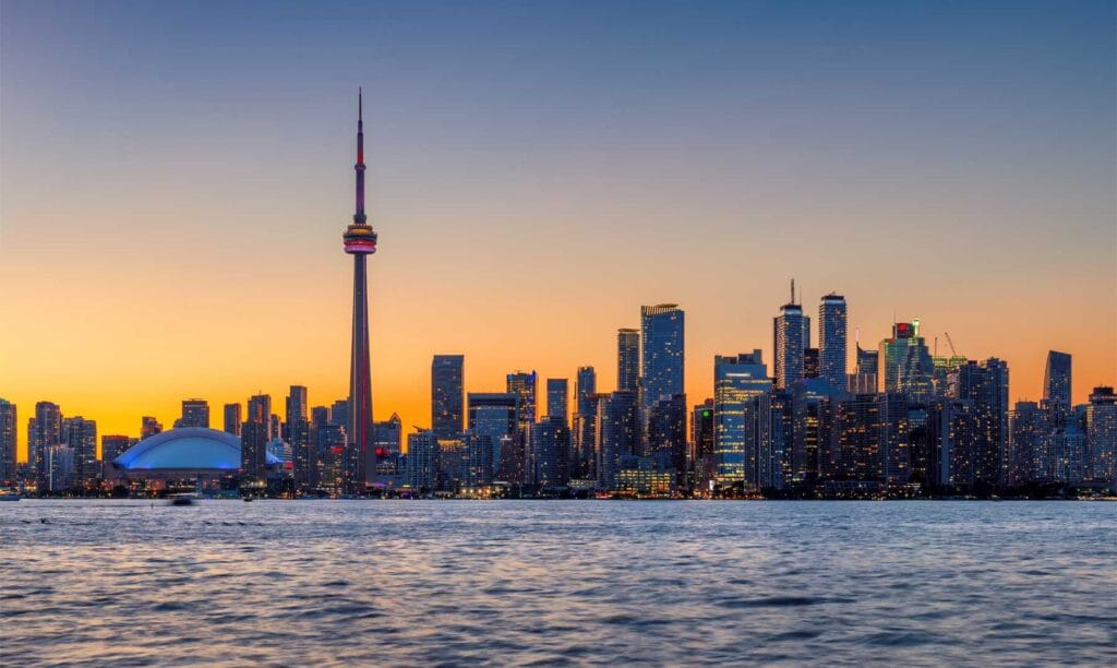 Skyline de Toronto ao entardecer com a CN Tower em destaque e reflexo das luzes no lago Ontário.