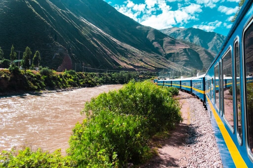 Trem azul passando ao lado do Rio Urubamba, com montanhas andinas ao fundo