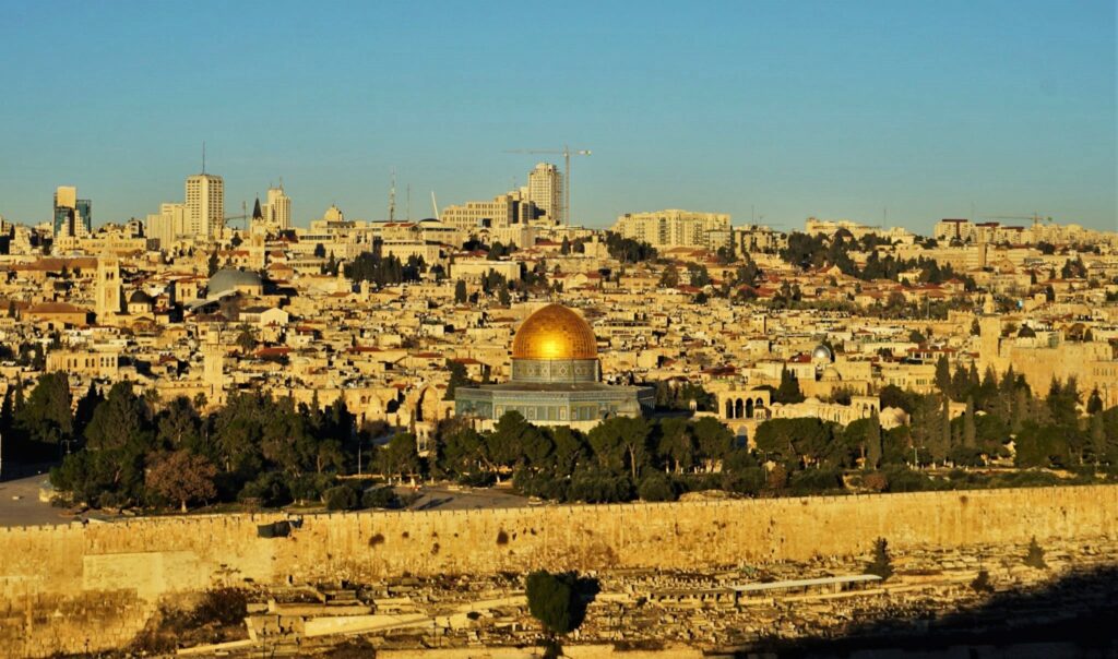 Vista panorâmica da Cidade Velha de Jerusalém com destaque para a Cúpula da Rocha ao entardecer.