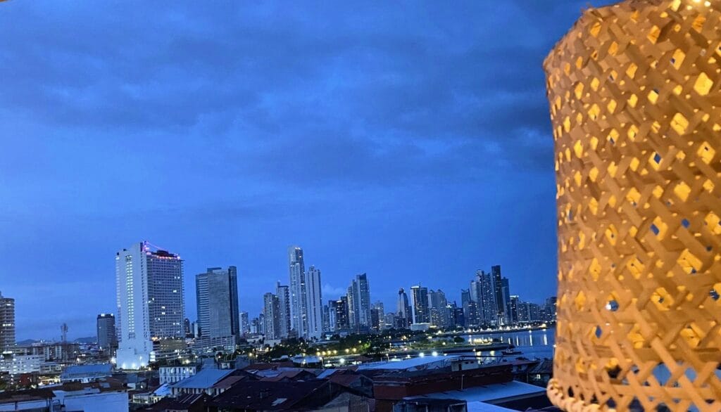 Skyline iluminado da Cidade do Panamá visto de um rooftop com detalhe de luminária artesanal em primeiro plano
