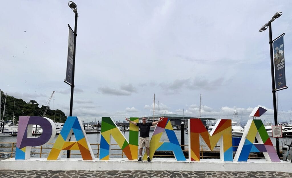 Viajante posando em frente ao letreiro colorido “Panamá” na Marina de Amador, com barcos ao fundo