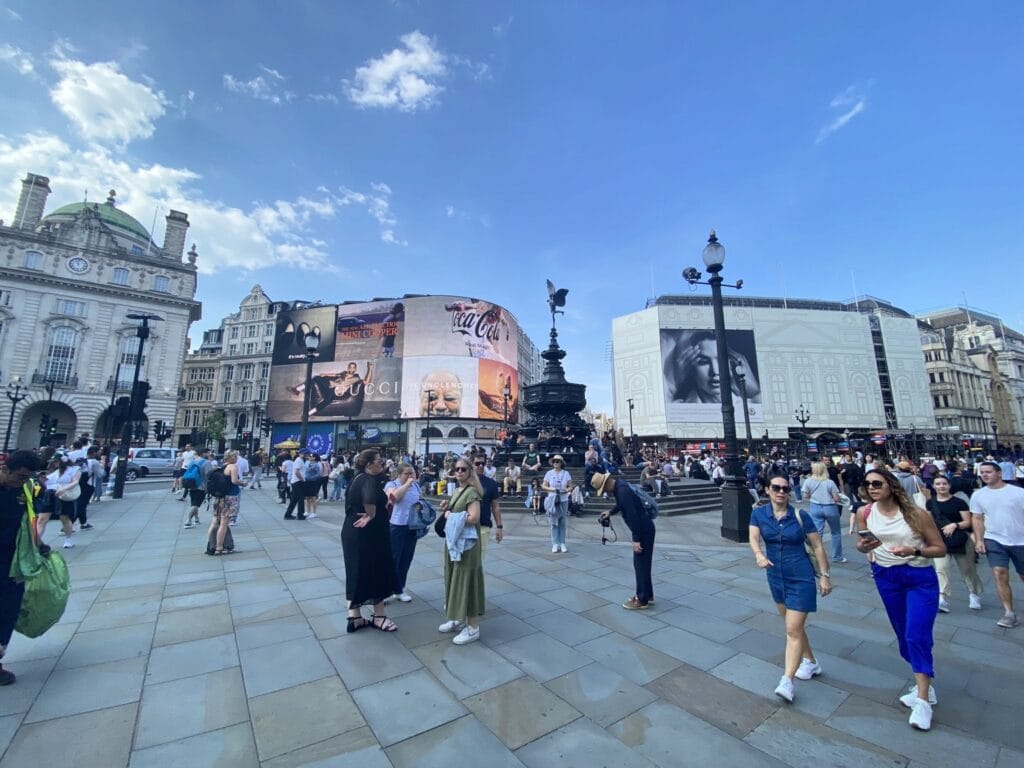 Pessoas circulando pela Piccadilly Circus em uma tarde de céu azul em Londres