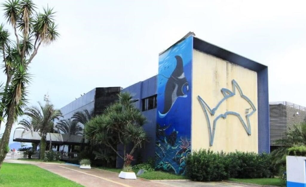 Fachada do Aquário Municipal de Santos com arte de tubarão e raia marinha, cercado por jardins tropicais – melhores pontos turísticos de Santos.
