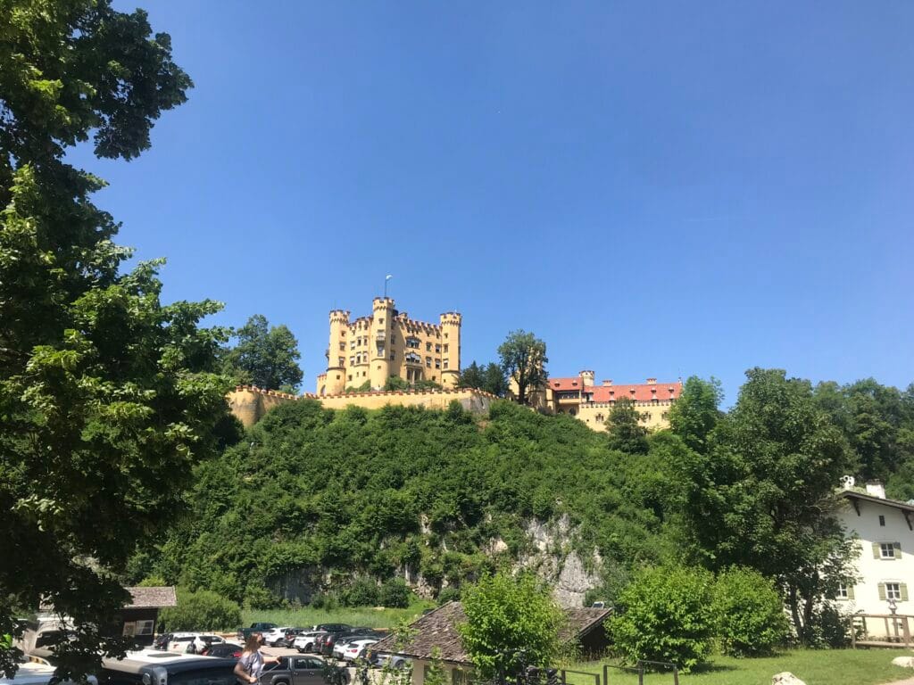 Castelo de Hohenschwangau no alto de uma colina verdejante, com céu azul ao fundo, localizado na região da Baviera, Alemanha. Bate e volta ao Castelo de Neuschwanstein.