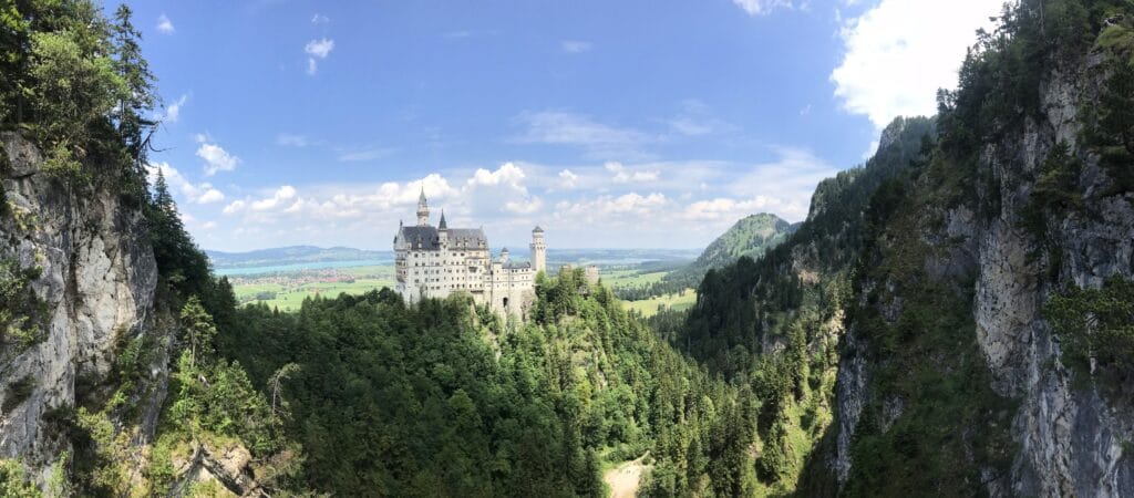 Vista panorâmica do Castelo de Neuschwanstein cercado por montanhas e florestas, fotografado da ponte Marienbrücke, na Alemanha. Bate e volta ao Castelo de Neuschwanstein.