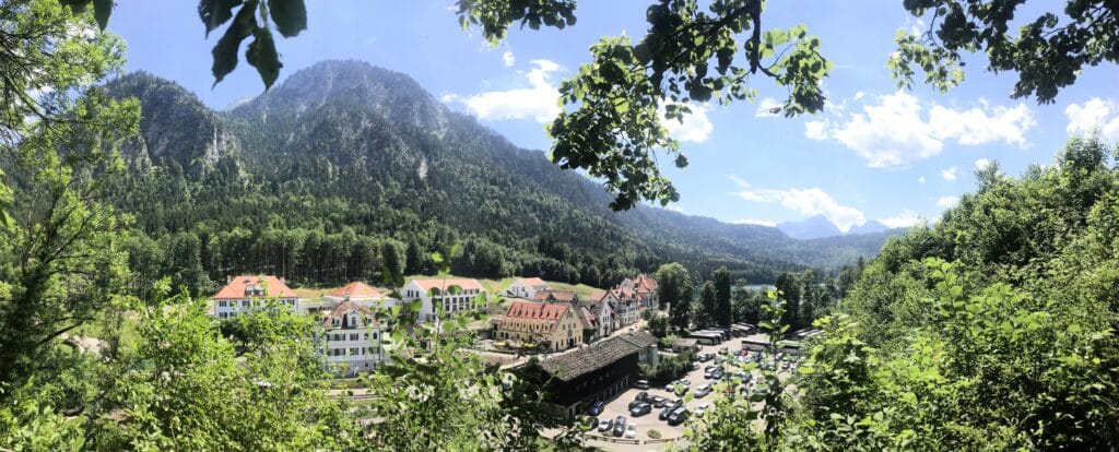 Panorama da vila de Hohenschwangau com telhados vermelhos, cercada por florestas e montanhas, vista da trilha de acesso ao Castelo de Neuschwanstein. Bate e volta ao Castelo de Neuschwanstein.