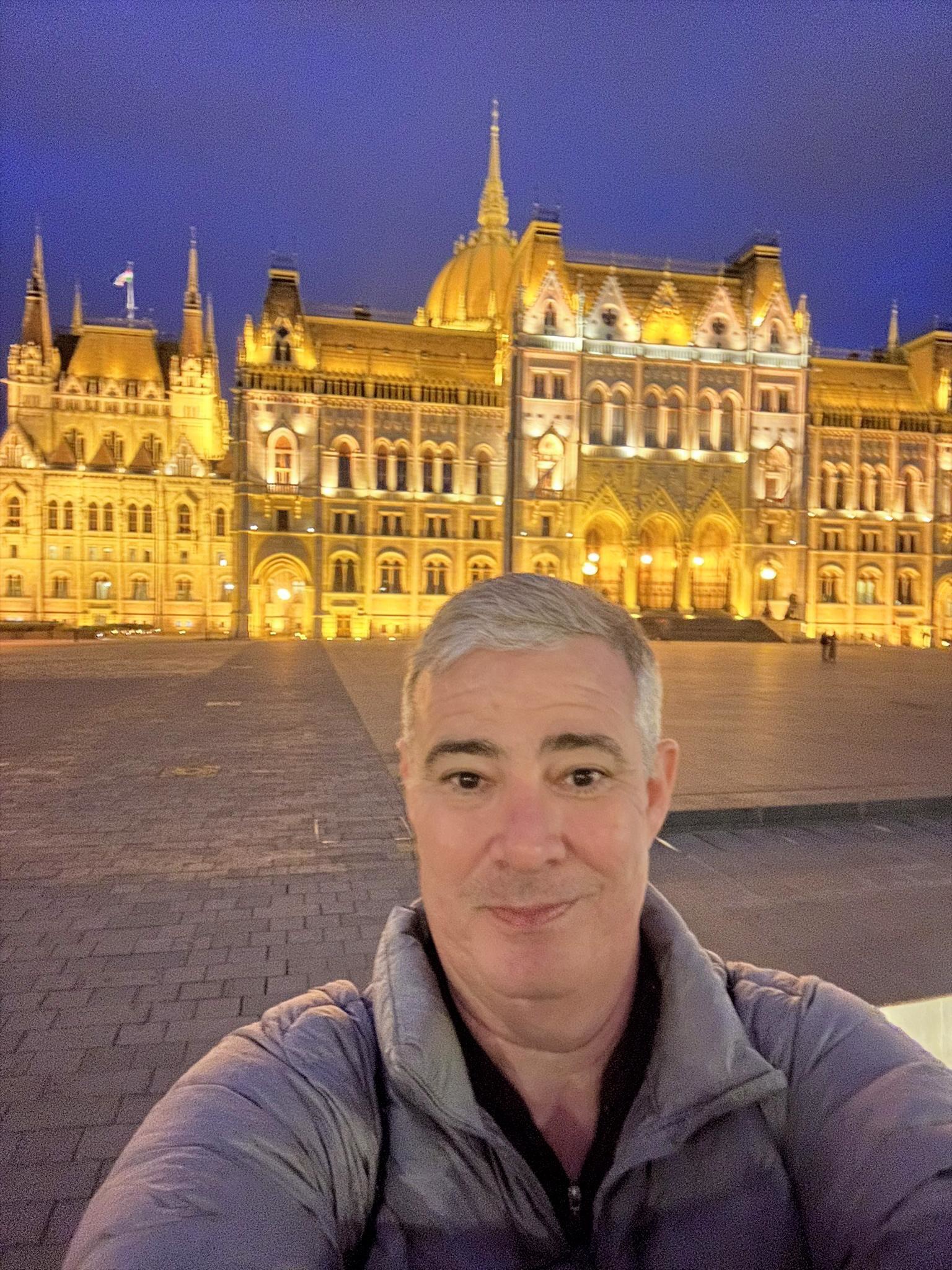 Selfie do Carlos Jantsch em frente ao Parlamento de Budapeste iluminado à noite, na Praça Kossuth Lajos, Hungria.